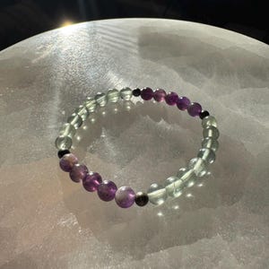 May include: A green and purple beaded bracelet with a silver accent bead.