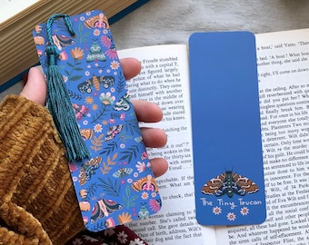 May include: Two blue and white bookmarks. One features a colorful floral pattern with butterflies and the other has a single, large, brown and orange moth with the text "The Tiny Toucan".