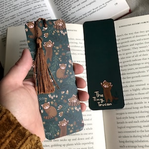 May include: Two bookmarks with a dark green background and a floral pattern. One bookmark features red pandas and the text "The Tiny Toucan". The other bookmark is solid dark green.