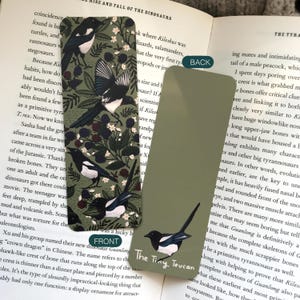 May include: Two rectangular bookmarks. One features a magpie bird design with berries and foliage on a dark green background. The other bookmark is solid olive green with a magpie illustration and the text "The Tiny Toucan".