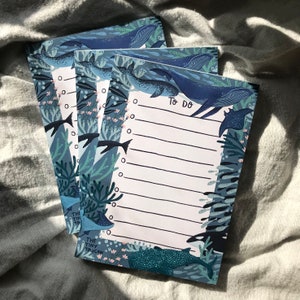 May include: A stack of four "To Do" list notepads with an ocean-themed design. The notepads feature illustrations of whales, fish, and coral in shades of blue and green. Each notepad has a lined section for writing and a header that says "To Do".