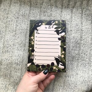 May include: A rectangular To Do list notepad with a green border, featuring illustrations of black and white magpie birds, white flowers, and blackberries. The notepad has lined spaces for writing tasks and the words "To Do" at the top.