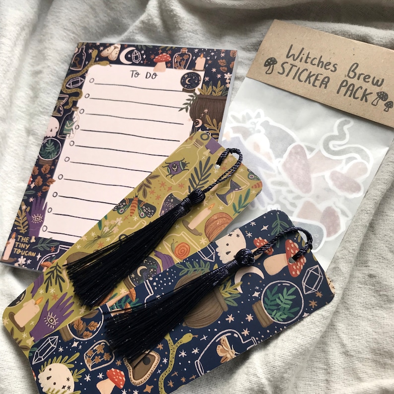 May include: A selection of witch-themed stationery. The image shows a notepad with "To Do" text, two bookmarks with black tassels, and a sticker pack. The items feature illustrations of mushrooms, moons, and potion bottles.