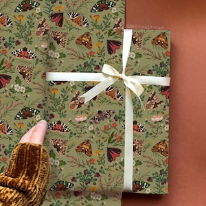 May include: Green gift wrap with a white ribbon and bow. The wrap features a repeating pattern of moths and flowers. The text "@thetinytoucan" is printed on the wrap.