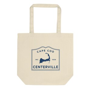 May include: A beige tote bag with a blue graphic of a map of Cape Cod, with the text "Cape Cod Inc 1639 Centerville".