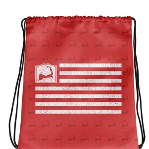 May include: Red drawstring bag with a white distressed American flag design featuring a silhouette of Cape Cod. The bag is covered in a repeating pattern of the Cape Cod silhouette.