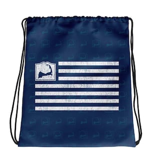 May include: A blue drawstring bag with a white distressed American flag design featuring a silhouette of the island of Martha's Vineyard. The bag is covered in a repeating pattern of the Martha's Vineyard silhouette.