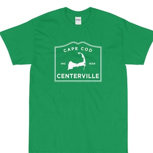 May include: Green short-sleeved t-shirt with a white graphic of a vintage-style logo that says "Cape Cod Inc. 1639 Centerville" with an outline of Cape Cod.
