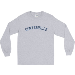 May include: A pale grey long-sleeved shirt featuring the word "CENTERVILLE" in navy blue, arched across the chest. The shirt has a crew neck and long sleeves.