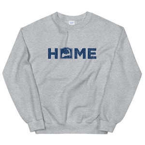 Op de afbeelding: Een grijs sweatshirt met het woord "HOME" bedrukt in blauw. De "O" in "HOME" is vervangen door een omtrek van de staat Massachusetts.
