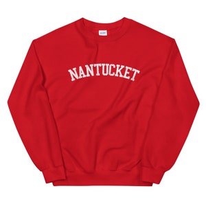 May include: A red sweatshirt with the word "NANTUCKET" printed across the chest in white, arched lettering. The sweatshirt has a crew neck and long sleeves. The Gildan brand label is visible at the back of the neck.