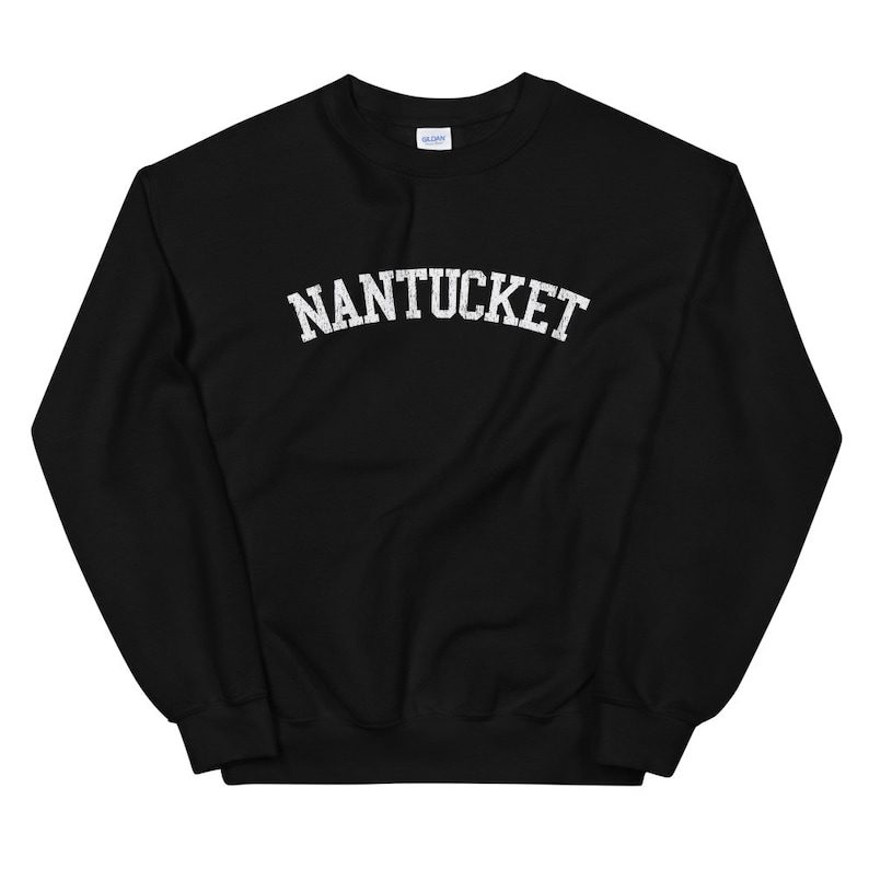 May include: Black crew neck sweatshirt with the word "NANTUCKET" printed across the chest in white, distressed-style lettering. The sweatshirt has a classic, casual design, suitable for everyday wear.
