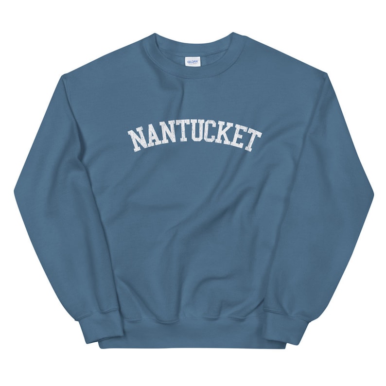 May include: A blue-grey sweatshirt with the word "NANTUCKET" printed across the chest in white, arched lettering. The sweatshirt has a crew neck and long sleeves. The fabric appears soft and comfortable.