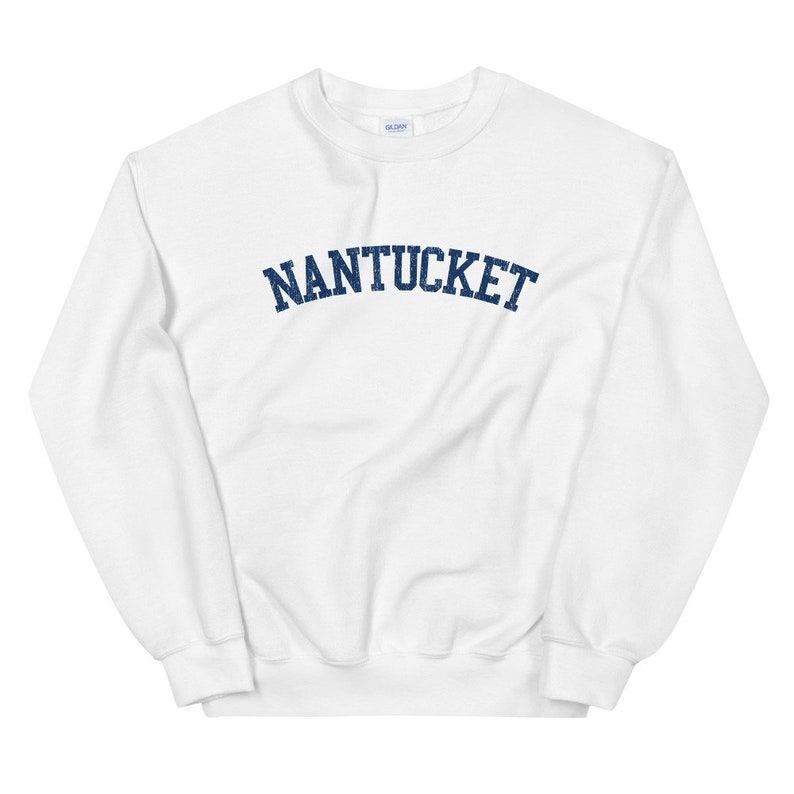 May include: White crew neck sweatshirt with the word "NANTUCKET" printed across the chest in navy blue, arched lettering. The sweatshirt is made of a soft material and has a classic, casual style.