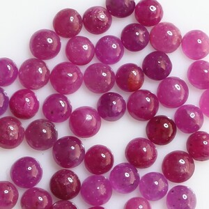 Könnte beinhalten: Eine Sammlung von 40 runden, rosafarbenen Rubin-Cabochons. Die Cabochons sind glatt und poliert, mit einer leichten Farbabweichung.