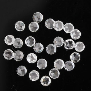 May include: A collection of 20 round, clear, faceted gemstones. The gemstones are arranged in a loose circle on a black background.