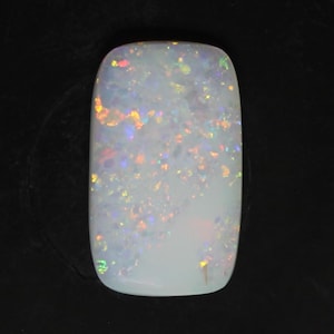 Könnte beinhalten: Ein rechteckiger, weißer Opal-Edelstein mit abgerundeten Kanten. Der Opal zeigt ein Farbspiel mit schillernden Blitzen in Orange, Gelb, Grün und Blau über seine gesamte Oberfläche. Der Edelstein ist vor einem schwarzen Hintergrund platziert.
