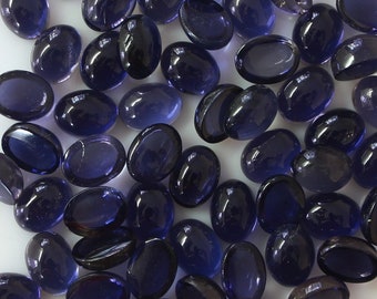 May include: A pile of 50 oval-shaped, dark blue, gemstone cabochons. The cabochons are smooth and polished.