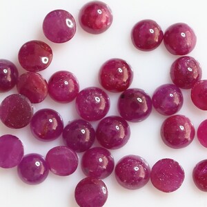 Könnte beinhalten: Eine Sammlung von 25 runden, cabochon geschliffenen Rubinen. Die Rubine sind tiefrot und haben eine glatte, polierte Oberfläche.