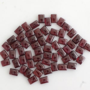 Könnte beinhalten: Ein Haufen von 50 losen, rechteckigen, roten Granatsteinen. Die Edelsteine sind facettiert und haben eine glänzende Oberfläche.