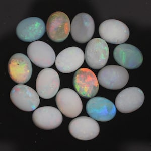 May include: A collection of oval-shaped opals in various shades of white, with some showing iridescent rainbow colours.