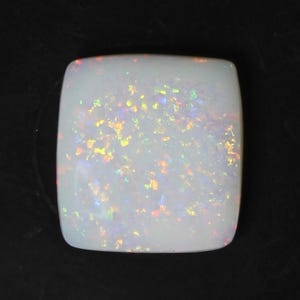 May include: A square, white opal gemstone with rounded corners. The opal displays a play-of-color effect with flashes of yellow, orange, and purple. The gemstone is set against a black background.