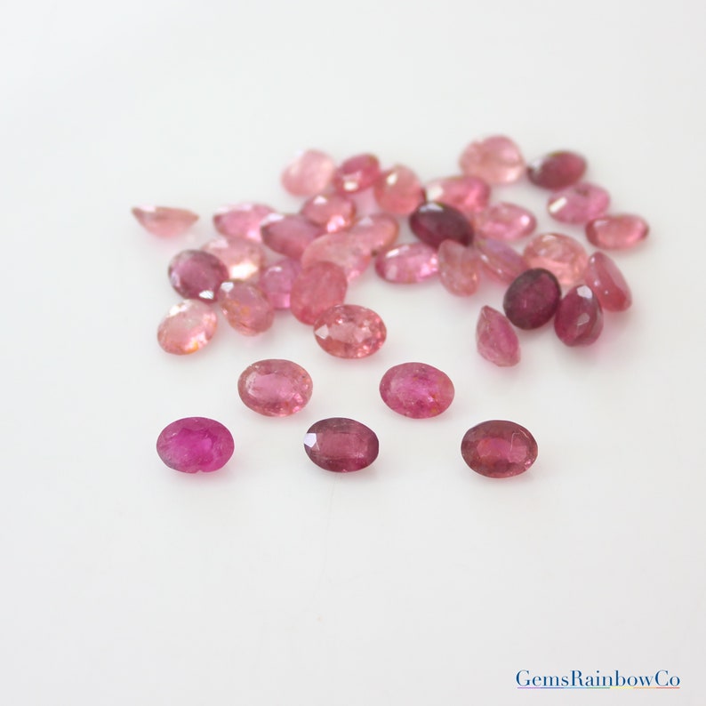 May include: A collection of pink oval-shaped gemstones. The gemstones are various shades of pink and have a faceted cut.