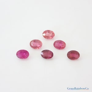 May include: Six oval-shaped pink gemstones, likely tourmalines, on a white background. The gemstones are various shades of pink, from light to dark.