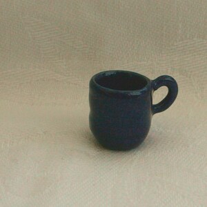 Peut inclure: Une petite tasse en céramique bleu foncé avec une anse arrondie.