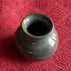 May include: A small, dark gray ceramic vase with a wide opening. The vase has a smooth, glossy finish and a slightly rounded shape.
