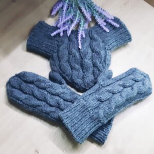 May include: A pair of blue knitted mittens with a cable knit pattern. The mittens are folded together and have a matching blue knitted hat.