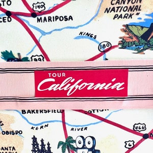 Pu&ograve; includere: Una mappa vintage della California con strade rosse, nomi di citt&agrave; e illustrazioni di punti di riferimento. La mappa include il testo "TOUR California" in uno striscione rosso. La mappa presenta illustrazioni di montagne, una cinepresa e un castello.