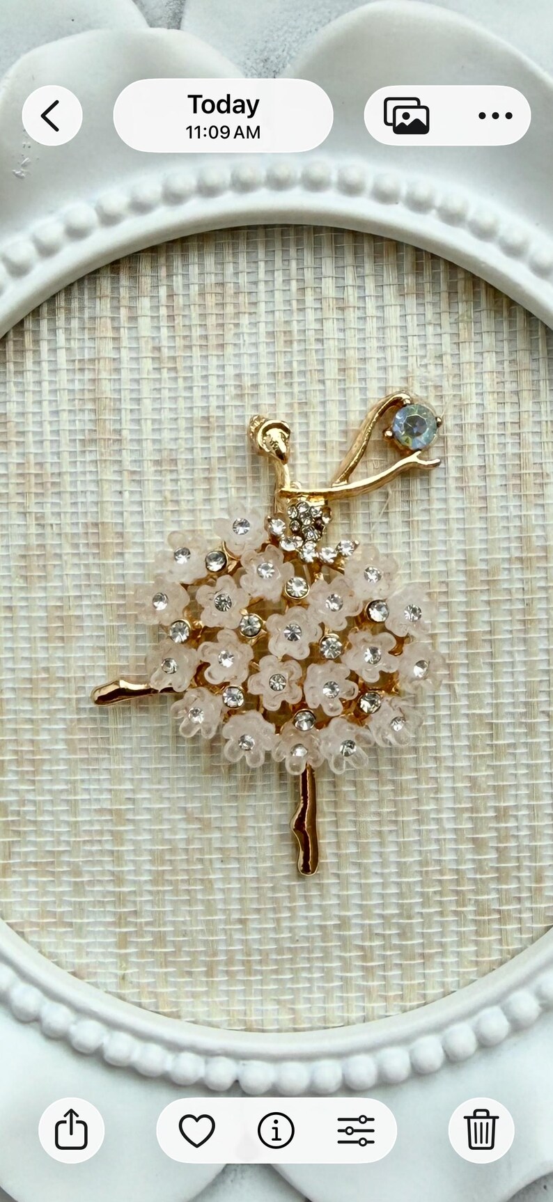 May include: A gold-toned ballerina brooch featuring a tutu made of translucent pale pink flower petals and clear rhinestones. The figure has a slender gold body, one arm raised with a single blue-tinted stone, and one leg extended.