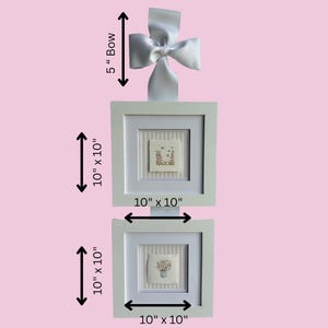 Pu&ograve; includere: Due opere d'arte quadrate incorniciate, ciascuna di 25,4 cm per 25,4 cm, con ricami floreali su sfondo a righe. Un fiocco bianco di 12,7 cm &egrave; attaccato in alto. Le cornici sono bianche e lo sfondo &egrave; rosa.