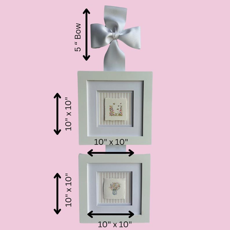 Pu&ograve; includere: Due opere d'arte quadrate incorniciate, ciascuna di 25,4 cm per 25,4 cm, con ricami floreali su sfondo a righe. Un fiocco bianco di 12,7 cm &egrave; attaccato in alto. Le cornici sono bianche e lo sfondo &egrave; rosa.