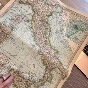 Puede incluir: Un mapa vintage de Italia con marcas detalladas de ciudades, pueblos y caracter&iacute;sticas geogr&aacute;ficas. El mapa est&aacute; impreso en papel de color crema con acentos marrones y verdes. El mapa est&aacute; ligeramente curvado en los bordes.