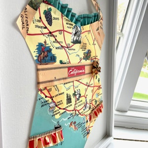 Pu&ograve; includere: Opera d'arte incorniciata a forma di costume da bagno, con una mappa vintage della California. La mappa &egrave; gialla, verde e blu, con linee rosse. Rifiniture a balze e un cinturino.