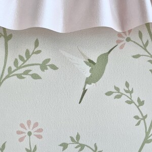 May include: A white background with a green hummingbird and pink flowers. The background has a subtle texture.