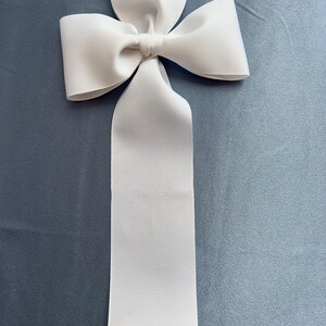 May include: A large white satin bow with a long tail. The bow is tied in a classic knot and is perfect for adding a touch of elegance to any occasion.
