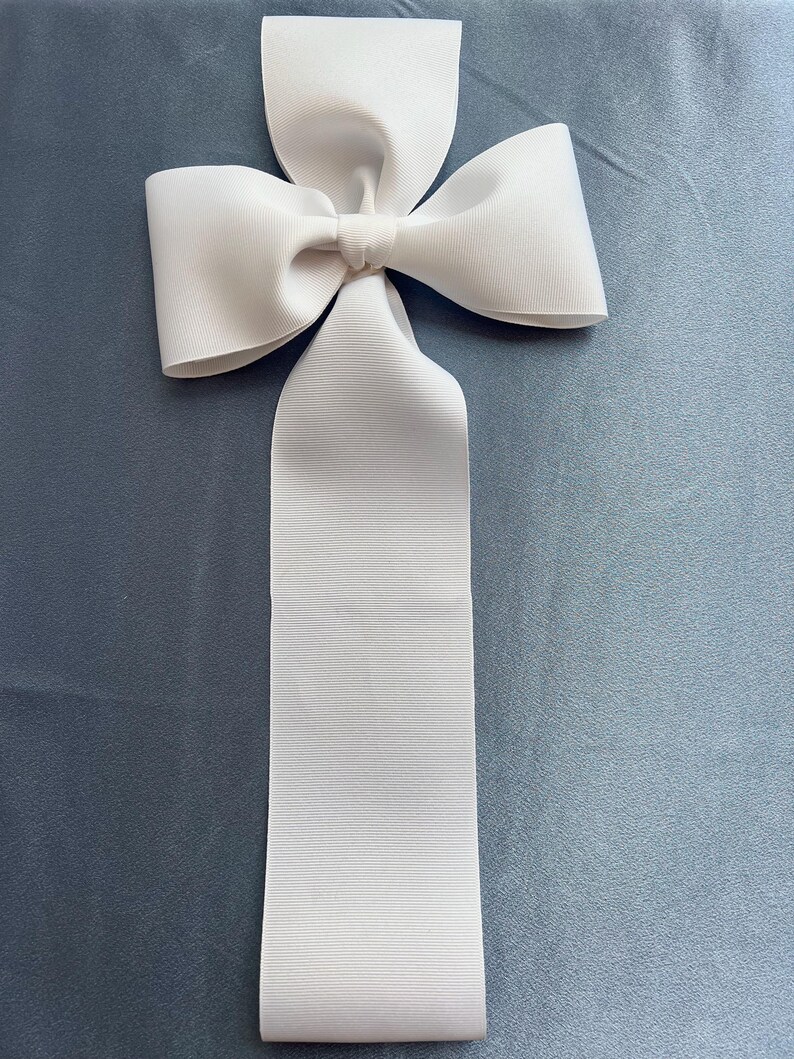 May include: A large white satin bow with a long tail. The bow is tied in a classic knot and is perfect for adding a touch of elegance to any occasion.