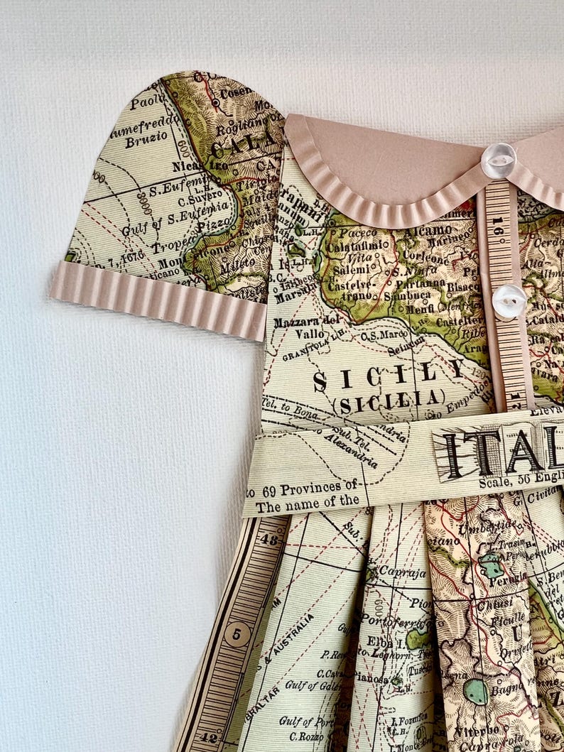 Puede incluir: Un vestido de estilo vintage hecho a partir de un mapa de Italia. El vestido tiene un corpi&ntilde;o marr&oacute;n con un cuello blanco y botones. La falda est&aacute; hecha de un mapa de Italia con las palabras "Italia" y "Sicilia" visibles. El vestido est&aacute; decorado con una cinta marr&oacute;n y una regla.