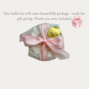 May include: A round object wrapped in clear bubble wrap, secured with a wide, light pink satin ribbon tied in a bow. A circular gold sticker with the text Gallivant Decor is attached. A small pink gift box icon is visible in the corner.