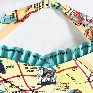 Pu&ograve; includere: Una borsa tote fatta a mano con un design a mappa vintage e un bordo a balze azzurro chiaro. La mappa include luoghi come lo Yosemite National Park e il Golden Gate Bridge. I cinturini della borsa sono realizzati con una stampa di mappa abbinata.