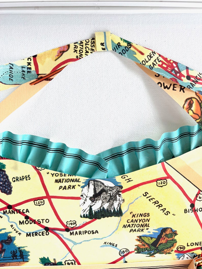 Pu&ograve; includere: Una borsa tote fatta a mano con un design a mappa vintage e un bordo a balze azzurro chiaro. La mappa include luoghi come lo Yosemite National Park e il Golden Gate Bridge. I cinturini della borsa sono realizzati con una stampa di mappa abbinata.