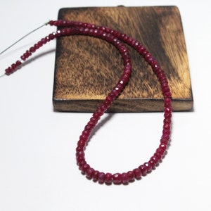 Puede incluir: Una hebra de cuentas de rubí rojo oscuro sobre una superficie de madera. Las cuentas son facetadas y tienen un acabado pulido.