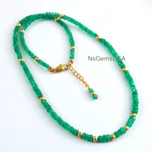 May include: A green gemstone necklace with gold beads. The necklace is made of faceted green gemstones and gold beads. The necklace has a lobster clasp closure and an extender chain.