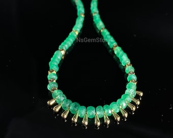 May include: A green emerald gemstone necklace with gold accents. The necklace is made of small, round beads and has a delicate, feminine look.