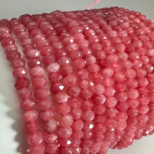 Pode incluir: Um fio de contas de pedra preciosa facetada rosa. As contas são redondas e têm um acabamento liso e polido.