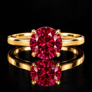 May include: A gold ring featuring a large, round, faceted deep red gemstone held in place by four prongs. The band is smooth and polished gold, reflecting light against a dark background, creating a clear mirror image below the ring.