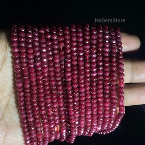 May include: A strand of deep red ruby beads, faceted and polished, with a high-gloss finish. The beads are strung on a clear thread and are approximately 4mm in diameter.